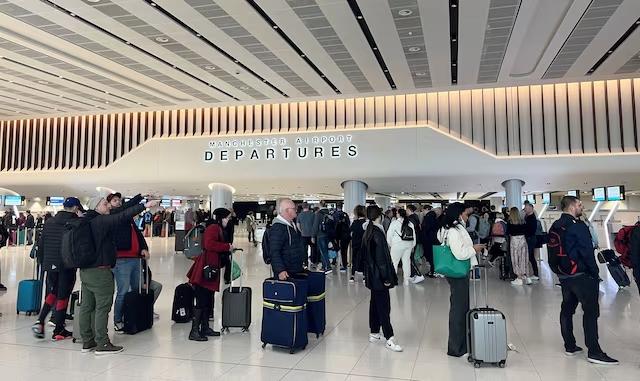 A group of people stands in an airport with their luggage, some checking details about United Airlines' refund policy.